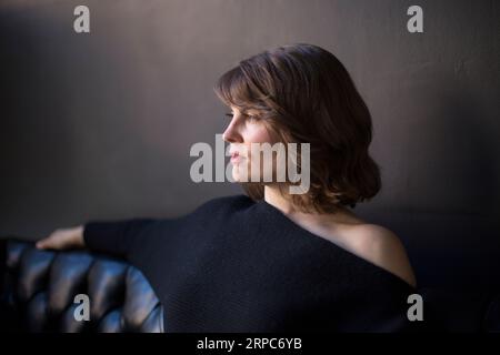 Eine junge Frau sitzt auf einer Couch und schaut von der Kamera weg Stockfoto