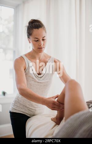 Eine junge Massagetherapeutin arbeitet an den Beinen eines Patienten Stockfoto