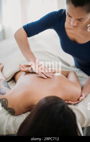 Eine junge Massagetherapeutin arbeitet an einem Knick im Rücken eines Patienten Stockfoto