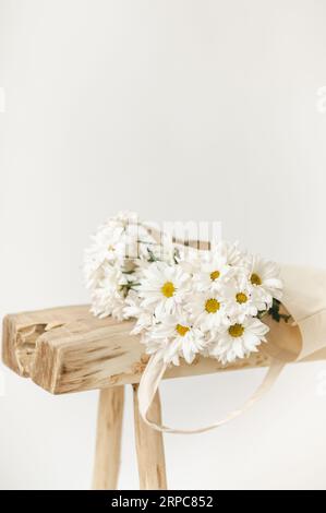 Blumenstrauß mit Gänseblümchen auf natürlicher Holzbank auf weißem Hintergrund Stockfoto