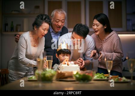 Ein kleiner asiatischer Junge, der sich wünscht, während die Familie in drei Generationen zu Hause seinen Geburtstag feiert Stockfoto