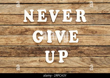 Geben Sie niemals auf, Wörter aus Holzbuchstaben auf einem hölzernen Hintergrund. Stockfoto