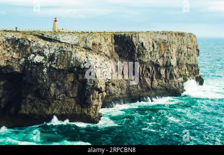 Ein atemberaubender Blick aus der Luft auf eine felsige Felsformation mit Blick auf das Meer, mit einem rot-weißen Leuchtturm am Rand Stockfoto