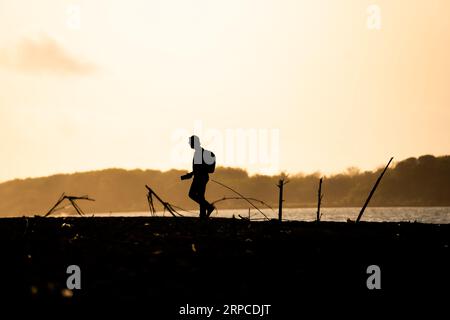 Silhouette eines Abenteurers, der an der Küste entlang spaziert und Fotos macht, Blick auf den Sonnenuntergang. Motivationskonzept. Stockfoto