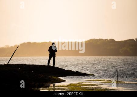 Silhouette eines Abenteurers, der an der Küste entlang spaziert und Fotos macht, Blick auf den Sonnenuntergang. Motivationskonzept. Stockfoto