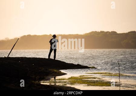 Silhouette eines Abenteurers, der an der Küste entlang spaziert und Fotos macht, Blick auf den Sonnenuntergang. Motivationskonzept. Stockfoto