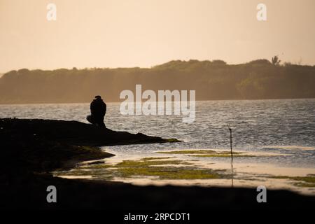 Silhouette eines Abenteurers, der an der Küste entlang spaziert und Fotos macht, Blick auf den Sonnenuntergang. Motivationskonzept. Stockfoto
