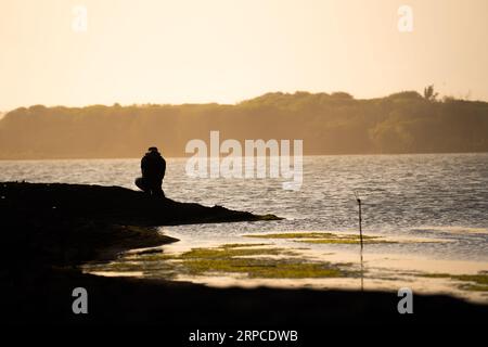 Silhouette eines Abenteurers, der an der Küste entlang spaziert und Fotos macht, Blick auf den Sonnenuntergang. Motivationskonzept. Stockfoto