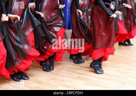Volkstanz. Traditionelles kaukasisches Volkstracht. Eine Reihe tanzender weiblicher Beine auf der Bühne. Beine in schwarzen Schuhen und Frauenhände mit rotem skir Stockfoto