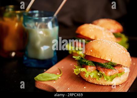 Frühstück mit Fischburgern und Kaffee. Gesunde Alternative zum klassischen amerikanischen Hamburger - Fischburger mit Lachs, Gurken, Tomaten und Salat. Stockfoto