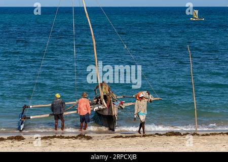 ANAKAO, MADAGASKAR - 24. NOVEMBER 2022: Mans entladen das auslegergeschnitzte Kanu, um Güter von Toliara nach Anakao zu transportieren. Traditionelles malagassisches Boot Stockfoto