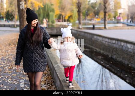 Glückliche Familie auf Herbstspaziergang. Mutter und Tochter spazieren im Park und genießen die wunderschöne Herbstlandschaft gemeinsam Stockfoto