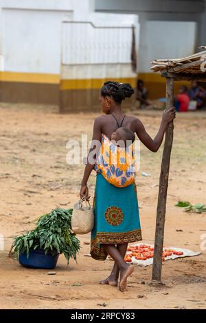 Bekopaka, Madagaskar - 6. November 2022: Madagassische Frau geht die Straße entlang mit einem Kind auf dem Rücken. Stockfoto