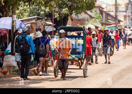 Mandoto, Madagaskar - 2. November 2022: Rikscha-Läufer stürzt mit einem kleinen Holzwagen durch die überfüllten Straßen. Eine handgeführte Rikscha, angetrieben von einem ru Stockfoto