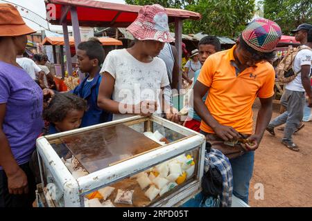 Mandoto, Madagaskar - 2. November 2022: Madagassischer Mann verkauft Milchprodukte aus einem einfachen Kühlkoffer auf der Straße von Mandoto. Stockfoto