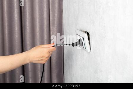 Das Mädchen zieht fälschlicherweise den Stecker aus der Steckdose und unterbricht die Steckdose. Stromschlaggefahr. Platz für Text kopieren Stockfoto