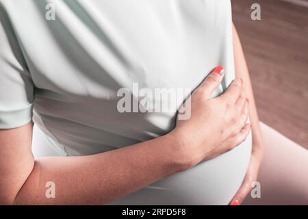 Eine schwangere Frau hält ihren Bauch im Solarplexus. Der Begriff der Pankreatitis-, Haltungs- und Belastungsschmerzen bei Schwangeren. Stockfoto