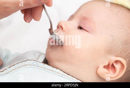 Eine Mutter aus einem Löffel gibt einem Kind wohltuende Tropfen für einen guten Schlaf, Nahaufnahme. Weinendes Baby Stockfoto