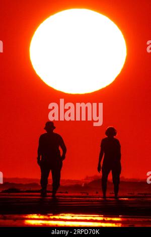 Isle Of Palms, Vereinigte Staaten. September 2023. Ein Paar spaziert den Strand entlang, der vom Sonnenaufgang umhüllt wird, während sie die Morgenruhe genießen, bevor die Massen am inoffiziellen Ende des Sommers, der vom Labor Day, 4. September 2023 in Isle of Palms, South Carolina, markiert wird. Quelle: Richard Ellis/Richard Ellis/Alamy Live News Stockfoto