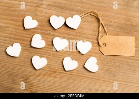 Weiße Holzherzen mit braunem Etikett auf einem Holztisch mit Kopierraum Stockfoto