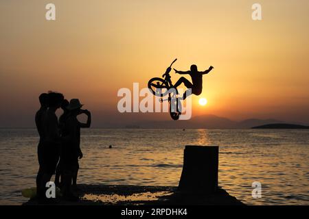 (190805) -- PEKING, 5. Aug. 2019 -- Menschen beobachten, wie ein Radfahrer mit seinem Fahrrad während des Water Jump BMX Day 2019 am Kavouri Beach in Athen, Griechenland, am 3. Aug. 2019 ins Meer springt. (Foto von /XINHUA) XINHUA FOTOS DES TAGES LEFTERISxPARTSALIS PUBLICATIONxNOTxINxCHN Stockfoto