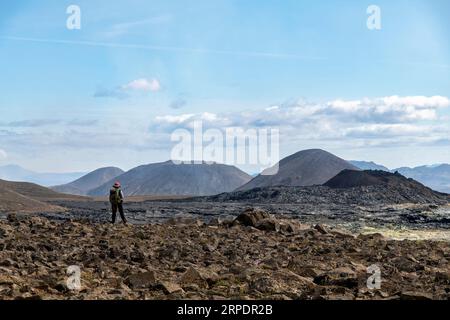 Stehende Frau mit Blick auf Lavafield in der Nähe des Berges Fagradalsfjall mit Spaltöffnung von 2021 im Vulkangebiet Geldingadalir südlich von Fagradalsfja Stockfoto