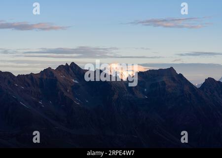 Blick auf den Mont Blanc vom Gletscher des Gran Paradiso Nationalparks bei Sonnenaufgang. Orange gelbe Spitze im Hintergrund, Berge und Tal im Schatten Stockfoto