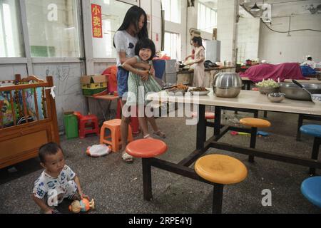 (190818) -- PEKING, 18. August 2019 -- Liu Lei hält ihre Schwester Liu Miao, während ihre Mutter Essen in der Kantine einer Kleiderfabrik in Shishi, Provinz Fujian im Südosten Chinas, am 2. August 2019 kocht. Die sengende Hitze hat Shishi im Südosten Chinas Fujian in diesem Sommer verschlingen lassen und nur wenige laufen auf den normalerweise geschäftigen Straßen. Im Gegensatz dazu sind die Kleiderfabriken, die in der Stadt dicht besiedelt sind, mit Menschen überfüllt, die von ihrer Arbeit überschwemmt wurden, da der Sommer die Hauptsaison für die Herstellung von Kleidungsstücken jedes Jahr ist, und auch ihre Kinder. Der Status von Shishi als Hauptkleidung Stockfoto