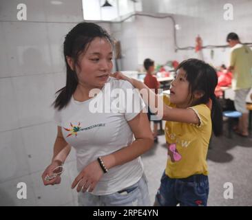 (190818) -- PEKING, 18. August 2019 -- Lu Changli knetscht ihre Mutter die Schultern, nachdem sie in der Kantine einer Kleiderfabrik in Shishi, südöstliche chinesische Provinz Fujian, am 1. August 2019 gegessen hat. Die sengende Hitze hat Shishi im Südosten Chinas Fujian in diesem Sommer verschlingen lassen und nur wenige laufen auf den normalerweise geschäftigen Straßen. Im Gegensatz dazu sind die Kleiderfabriken, die in der Stadt dicht besiedelt sind, mit Menschen überfüllt, die von ihrer Arbeit überschwemmt wurden, da der Sommer die Hauptsaison für die Herstellung von Kleidungsstücken jedes Jahr ist, und auch ihre Kinder. Der Ruf, Shishi sei ein wichtiger Kleiderschrank Stockfoto