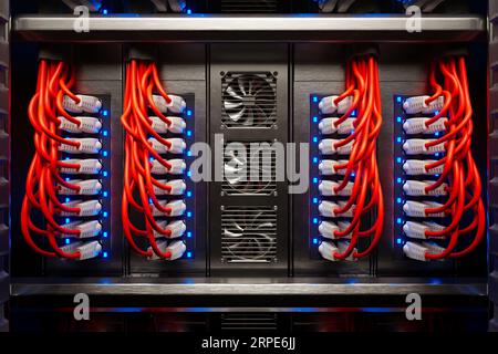 Viele rote Kabel und drehende Lüfter in einem Serverschrank, der von einem Scheinwerferlicht beleuchtet wird. Stockfoto