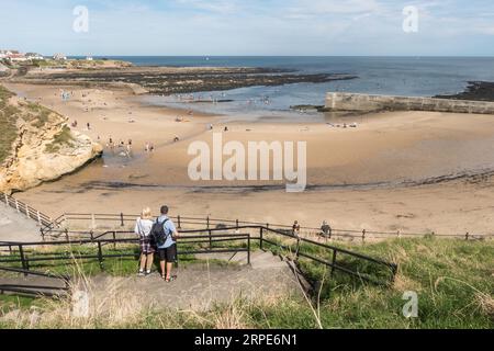Pärchen mit Blick auf Cullercoats Bay und Urlaubern am Strand und im Meer, England, Großbritannien Stockfoto