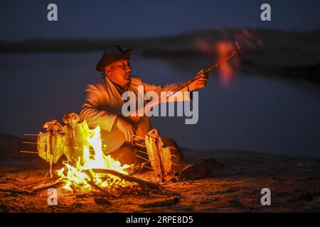 (190821) -- YULI, 21. August 2019 -- Amudun Abudu spielt ein Instrument in Lop nur People Village im Yuli County, nordwestchinesische Autonome Region Xinjiang Uygur, 11. April 2019. Lop nur People Village liegt im Yuli County, wo der Tarim River durch die Wüsten fließt, wobei die Populus euphratica Wälder die schimmernden Wellen reflektieren. Amudun Abudu, ein 61 Jahre alter typischer Dorfbewohner von Lop nur, arbeitet in der lokalen Tourismusbranche. Mit dem Wandel der Zeit haben viele Menschen in Lop nur verschiedene Lebensmöglichkeiten, doch er beharrt auf der Tradition des Fischens in Flüssen und Seen. Er macht nicht nur d Stockfoto