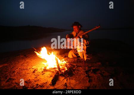 (190821) -- YULI, 21. August 2019 -- Amudun Abudu spielt ein Instrument in Lop nur People Village im Yuli County, nordwestchinesische Autonome Region Xinjiang Uygur, 11. April 2019. Lop nur People Village liegt im Yuli County, wo der Tarim River durch die Wüsten fließt, wobei die Populus euphratica Wälder die schimmernden Wellen reflektieren. Amudun Abudu, ein 61 Jahre alter typischer Dorfbewohner von Lop nur, arbeitet in der lokalen Tourismusbranche. Mit dem Wandel der Zeit haben viele Menschen in Lop nur verschiedene Lebensmöglichkeiten, doch er beharrt auf der Tradition des Fischens in Flüssen und Seen. Er macht nicht nur d Stockfoto