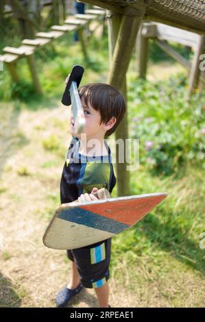 Junger kaukasischer Junge, der vorgibt, ein Ritter in einer Burg zu sein, während er mit einem Holzschwert und Schild spielt Stockfoto