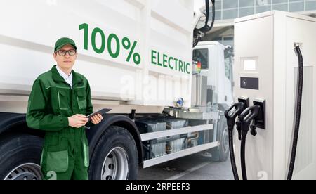 Manager mit einem digitalen Tablet neben Elektro-Müllwagen und ekektrischer Fahrzeugladestation. Stockfoto