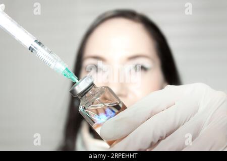 Die Krankenschwester zeigt Spritzenflüssigkeit aus der Durchstechflasche, indem sie auf den Kolben drückt, um Luft und Tropfen der Impfflüssigkeit abzulassen, um die korrekte Anwendung zu gewährleisten o Stockfoto