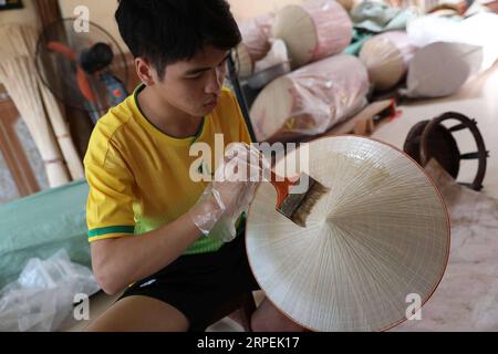 (190830) --, 30. August 2019 -- Ein junger Mann aus der Region malt am 29. August 2019 im Dorf Chuong am Stadtrand der vietnamesischen Hauptstadt einen traditionellen konischen Hut. Die traditionellen konischen Hüte Vietnams bestehen größtenteils aus Bambus und Palmblättern und gehören zu den beeindruckendsten traditionellen Kostümen des Landes. Die Menschen im Dorf Chuong stellen seit etwa 400 Jahren konische Hüte her. Die Einheimischen kaufen grüne Palmblätter aus anderen Provinzen, trocknen sie in der Sonne, bügeln sie und bleichen die Blätter in flache Scheiben. Sie fixieren dann mit dünnen Fäden Blattschichten auf einem Kegel aus Bambusringen. Stockfoto