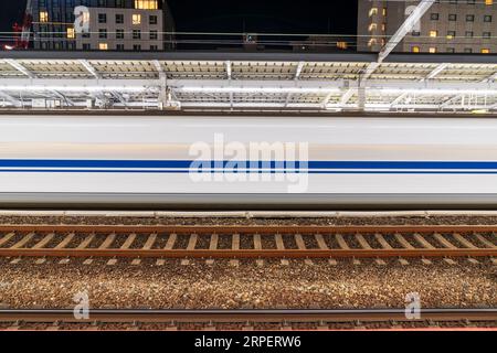 Ein japanischer Nozomi shinkansen-Zug, der nachts 200 km/h durch den Bahnhof Fukuyama fährt. Der Zug ist weiß, blau und grau verschwommen. Stockfoto