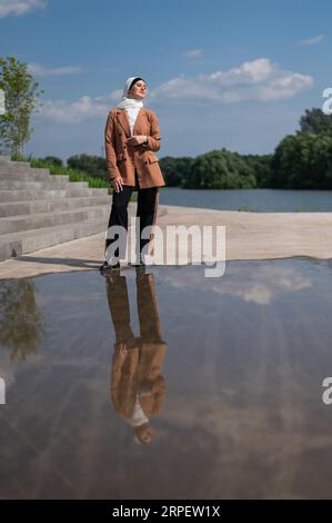 Eine junge Frau, die einen Hijab trägt, steht neben einer großen Pfütze. Stockfoto