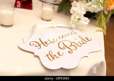 Ein eleganter Hochzeitstisch mit einem Holzschild mit der Aufschrift „Here comes the Bride“ in der Nähe einer beleuchteten Kerze Stockfoto
