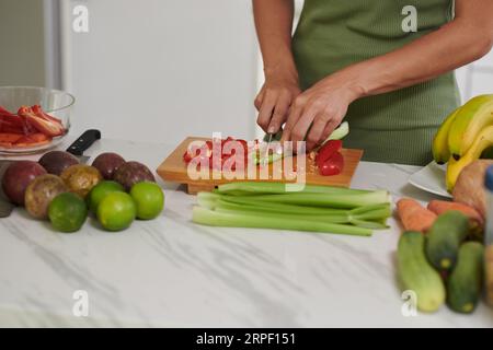 Hände einer jungen Frau, die frischen Sellerie und Paprika auf Holzbrett schneidet, während sie am Küchentisch steht und das Frühstück kocht Stockfoto