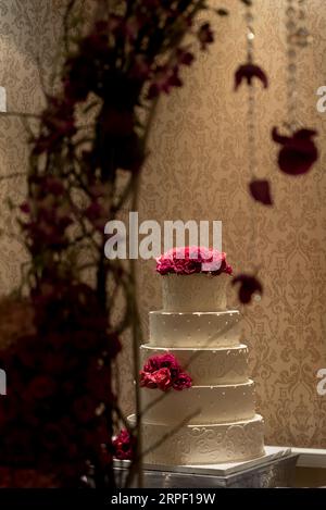 Weiße Hochzeitstorte mit rosa Blumen und einem weißen Spitzenmuster sitzt auf einer rosa und weiß gestreiften Tischdecke Stockfoto