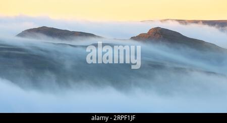 Gipfel der Smearsett Narbe, Ribblesdale, der bei Sonnenuntergang durch eine Nebel-/Wolkenumkehrung stochert, fotografiert über Langcliffe, Ribblesdale, Yorkshire Dales, North Stockfoto