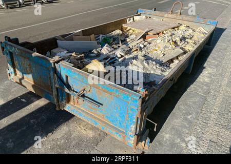 Müllcontainer aus Metall, gefüllt mit Bauschutt, Schutt in der Nähe einer Baustelle. Auf der Straße in Europa Stockfoto