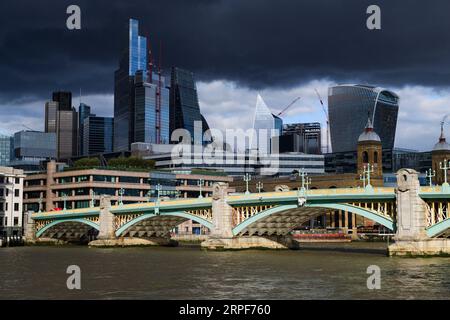 Sturmwolken erheben sich über den Wolkenkratzern des Finanzdistrikts City of London im Hintergrund der Southwark Bridge über der Themse. So Stockfoto