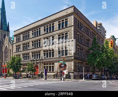 Upper West Side: School of the Holy Name of Jesus ist ein unsinniges, düsteres, graues Ziegel- und Steingebäude, das nur von bogenförmigen, rot bemalten Türen belebt wird. Stockfoto