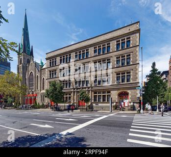 Upper West Side: School of the Holy Name of Jesus ist ein unsinniges, düsteres, graues Ziegel- und Steingebäude, das nur von bogenförmigen, rot bemalten Türen belebt wird. Stockfoto