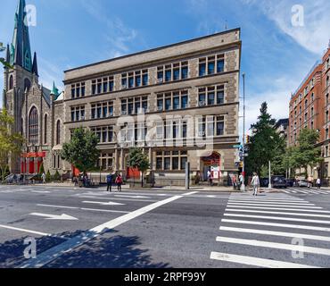 Upper West Side: School of the Holy Name of Jesus ist ein unsinniges, düsteres, graues Ziegel- und Steingebäude, das nur von bogenförmigen, rot bemalten Türen belebt wird. Stockfoto