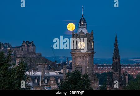 Skyline der Stadt mit blauem Supermond über dem Balmoral-Uhrenturm, Scott Monument und Edinburgh Castle, Schottland, Großbritannien Stockfoto