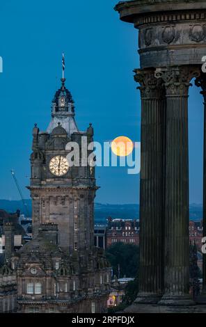 Skyline der Stadt mit blauem Supermond über dem Balmoral-Uhrenturm, Scott Monument, Edinburgh, Schottland, Großbritannien Stockfoto